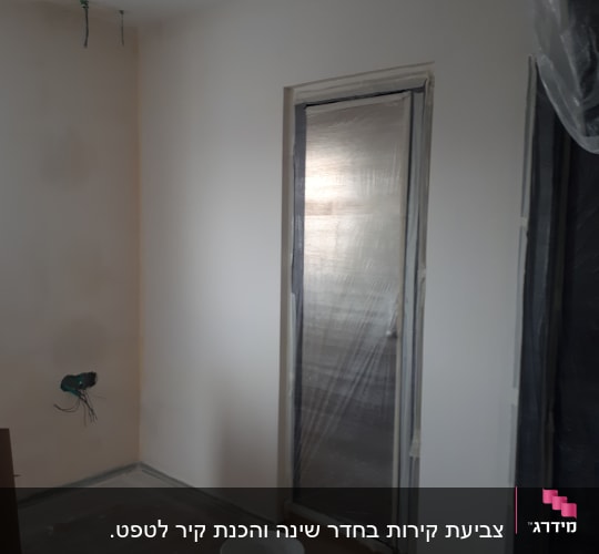 חדר צבוע עם דלת מכוסה בניילון, דלי צבע על הרצפה